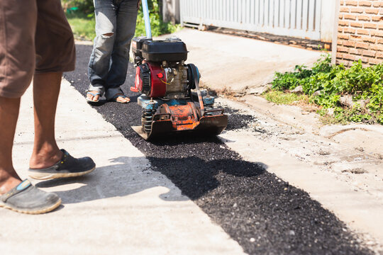 A worker using a plate compactor machine to flatten and solidify fresh asphalt on a road.