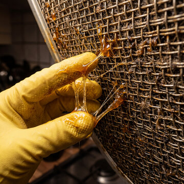 Photographie d'une main gant&eacute;e touchant la graisse visqueuse et collante accumul&eacute;e sur le filtre m&eacute;tallique d'une hotte de cuisine