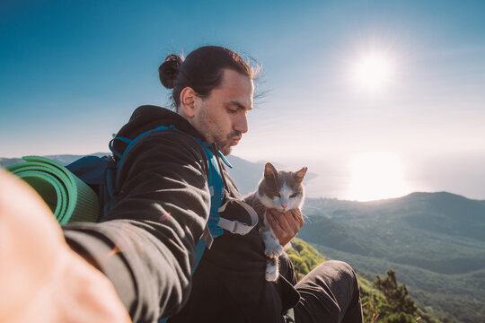 A man tourist with a cat makes a selfie in the mountains at dawn
