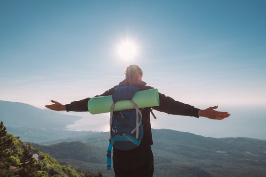 A tourist stands with his arms outstretched on top of a mountain at sunrise