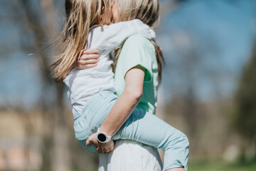 Fototapeta premium A mother carries her daughter in a close hug while standing outdoors. They share a tender embrace in a calm, casual moment.