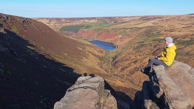 Drone POV of Man sitting on the highly exposed rock. The Trinnacle is a remote and highly exposed rock formation in the Peak District near the town of Oldham at around 900ft in altitude.