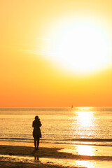 Fototapeta premium a woman silhouette on the beach against sunset orange sea and sky