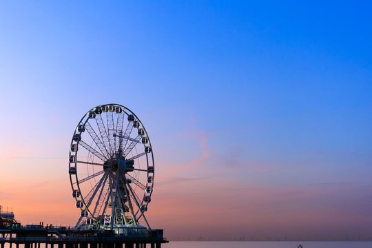 a ferries wheel with lighting on in the sunset orange blue sky, background image, text space, Den Haag, de Pier