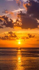 Obraz premium Vivid orange sunset over ocean, reflecting on the water with a boat silhouette in view