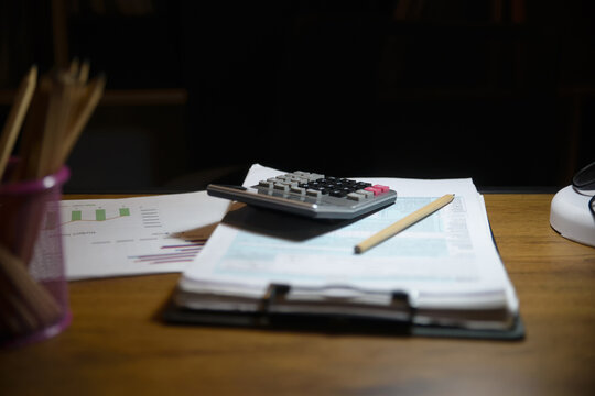 A calculator on financial documents and tax forms on a desk at night. This setup represents office accounting and paperwork management for business.