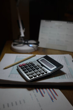 A calculator on financial documents and tax forms on a desk at night. This setup represents office accounting and paperwork management for business-vertical image