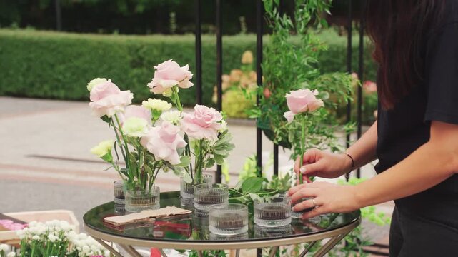 Elegant wedding floral display crafted. Delicate hands shape pastel blooms in vases. An artisan florist carefully designs and assembles delicate pastel flower displays in glass vases