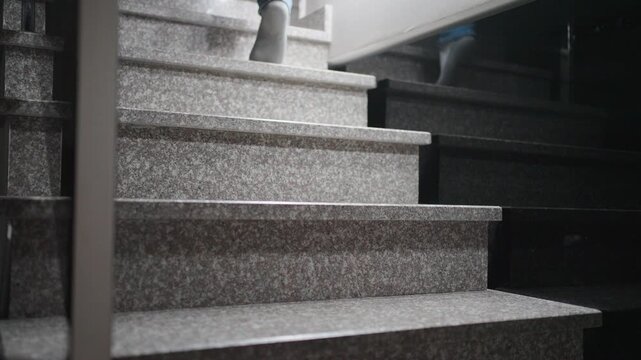 Close-up of Feet in Socks Walking Up Stone Stairs. Perspective shot of a person in jeans and white socks ascending marble steps at home. Concept of daily routine, movement, and domestic life
