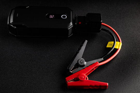 Portable car jump starter with power bank and alligator clips on black background