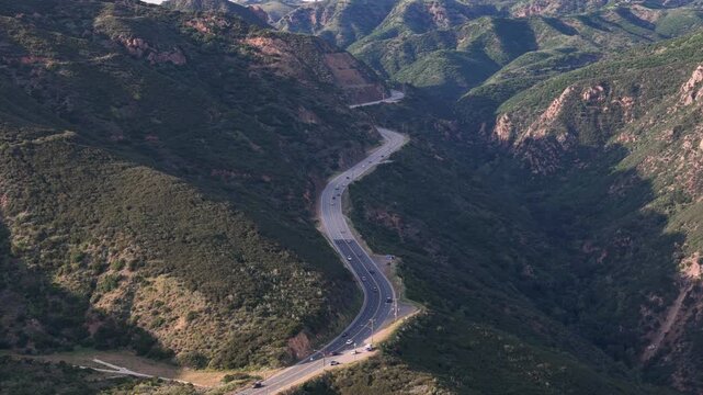 Aerial view of Kanan Dume road winding and cutting through the lush green mountains, the asphalt contrasting sharply with the dense vegetation, Malibu, California, United States.