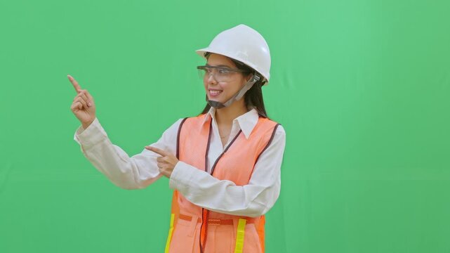 A female engineer in a white helmet pointing towards an imaginary safety sign. Directing attention to rules or procedures on a green screen background.