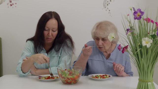 Ladies sampling food while engaging in conversation. Caucasian women sharing meal at decorated table. Two women of European descent enjoying salad amidst floral decor and gestures
