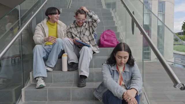 Students bullying and laughing at a sad lonely girl on campus stairs