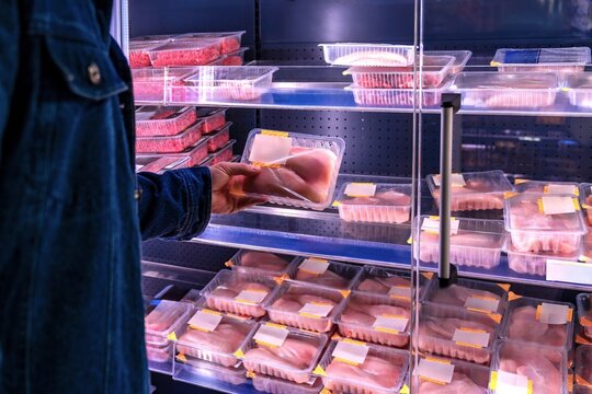 Grocery shopper selects meat products. Supermarket customer picks beef package under bright lights. Shopper examines packaged meat in refrigerated section during evening shopping trip