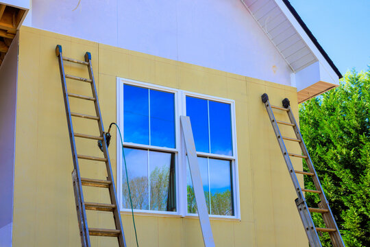 Ladders are leaned against side of house as workers plan to paint exterior after installing fiber siding
