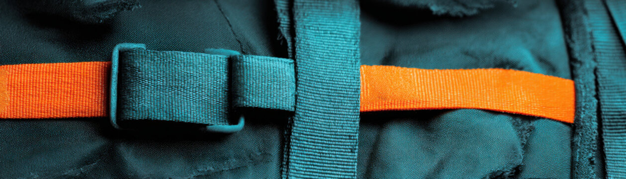Strap buckle fastening on fabric with orange and teal straps showing logistic fastening detail for secure transport and handling
