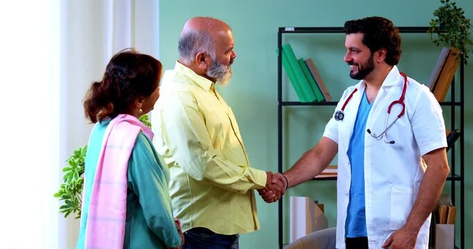 Professional Indian young male doctor and Asian senior retired couple patients shaking hands after successful treatment in a modern clinic; healthcare, recovery, and old age wellness concept.