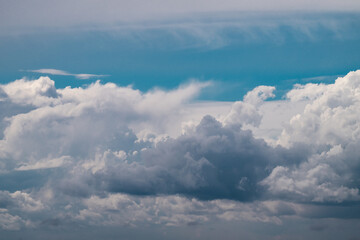 Naklejka premium a multi-layered sky featuring a dense wall of dark grey and white cumulus clouds at the bottom, set against a bright blue sky with soft, wispy cirrus cloud formations