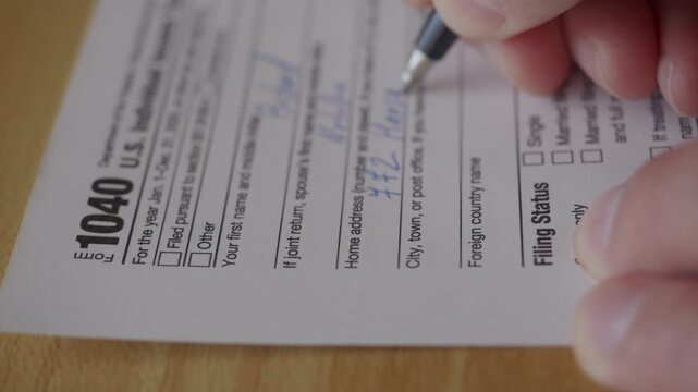 Man Filling In The Tax Form 1040. Person Calculates of Planning Budgets Yearly Personal Finance and Fills up US Tax Form 1040. Signing 1040 Income Tax Return. Names and numbers are fictitious.