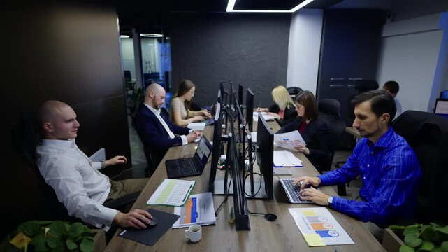 Business professionals actively engage in their daily tasks within a contemporary office setting. They are focused on their work, utilizing computers and reviewing various documents.