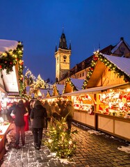 Naklejka premium A vibrant nighttime scene of a festive outdoor market, showcasing wooden stalls adorned with holiday decorations. People stroll about