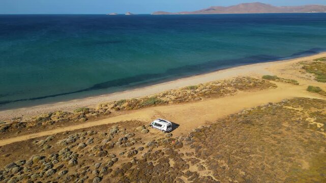 Aerial drone view of a parked campervan at beach Parthenomitos on Limnos Island, Greece. Remote Mediterranean coastal landscape with turquoise sea, rocky shoreline, and peaceful free camping