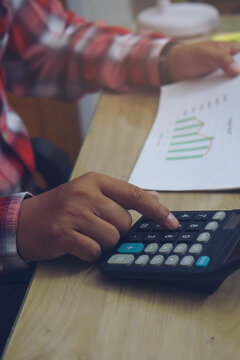 Business man hand planning and use caculator to calculate budget, work on laptop. Professional Businessman writing on paper and analysis annual report at home office-vertical image.