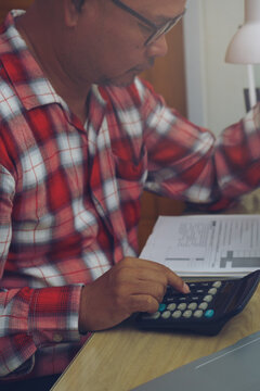 Business man hand planning and use caculator to calculate budget, work on laptop. Professional Businessman writing on paper and analysis annual report at home office-vertical image.