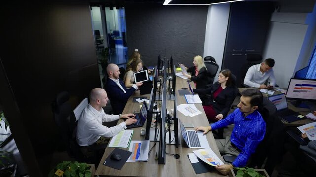 A busy team of professionals is actively engaged in their work within a modern office environment. Employees are focused on tasks, utilizing technology and documents at individual workstations.