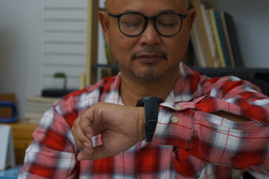 Businessman checking time and looking at smart wrist watch at home office.  Asian man seeing clock to work. Desk with laptop, annual, and summary report.Time out for appointment meeting