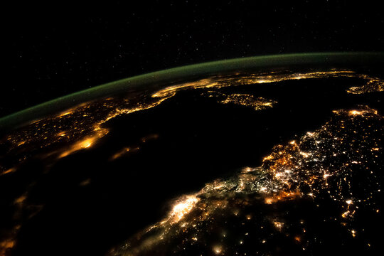 Satellite view of Mediterranean cities at night from space. ISS photo showing city lights, Earth curvature and green airglow. Elements furnished by NASA.