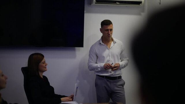 A business professional leads a meeting, presenting ideas to his diverse colleagues in an office. The team collaborates and discusses important strategies during this corporate presentation.