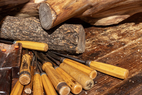 High angle shot of professional woodworking hand tools with wooden handles and raw timber logs on a distressed vintage workbench.