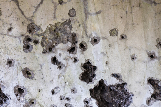 Concrete wall with bullet holes and cracks as damaged surface texture