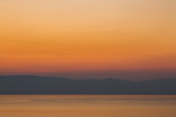 Obraz premium The sun rises over the mountains on the Greek mainland and reflects in the Ionian Sea on a beautiful cloudless morning taken from the island of Corfu