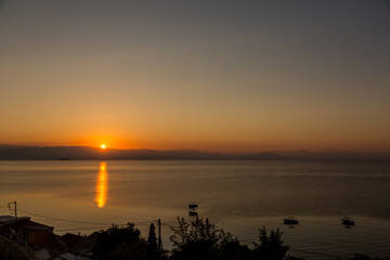 Obraz premium The sun rises over the mountains on the Greek mainland and reflects in the Ionian Sea on a beautiful cloudless morning taken from the island of Corfu