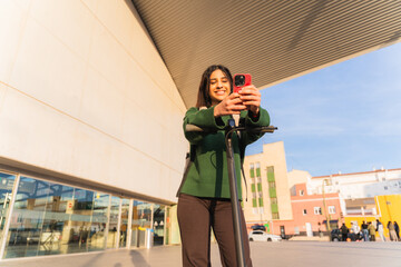 Young woman smiling, holding smartphone, and standing with electric scooter outdoors © pablo