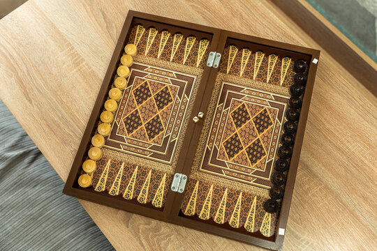 Ornate Backgammon Board With Gold Pieces, Carved Geometric Points And Glossy Finish, Warm Woodgrain Tabletop, Handcrafted Inlay Motifs, Tactile