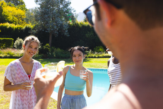 Smiling Diverse friends raising glasses by poolside in backyard, with pitcher of lemonade