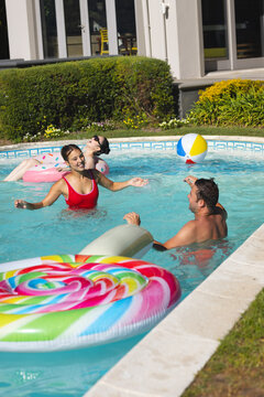 Diverse friends splashing around donut float in backyard pool, with beach ball drifting