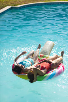 Kicking water with diverse female friends reclining on pool float in backyard pool with sunglasses