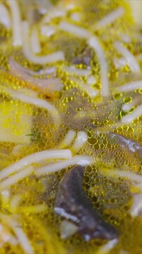 Golden mushroom noodle broth simmering gently rich umami soup with oil droplets, sliced mushroom pieces, thin noodles, potato cubes, warm kitchen glow, closeup simmering shot