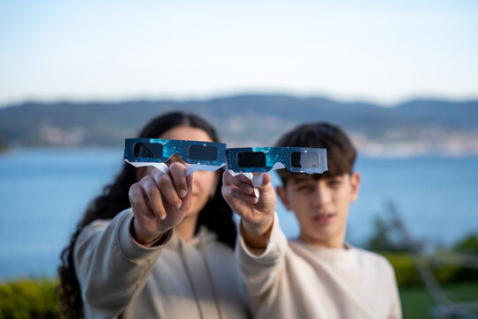 Teenagers showing solar eclipse glasses to camera outdoors
