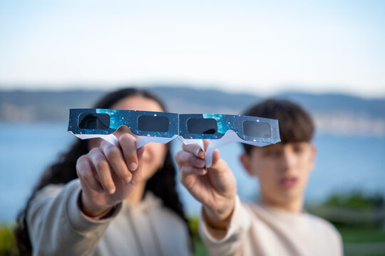 Teenagers showing solar eclipse glasses to camera outdoors