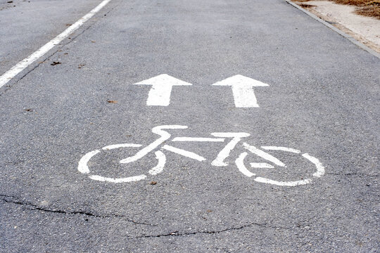 White bicycle lane marking and direction arrows on asphalt, cycling path symbol, road safety and traffic regulation sign.