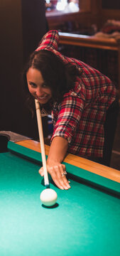 Woman in plaid leaning over pool table aiming cue near cue ball, ring visible in bar
