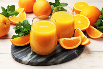 Citrus juice in glasses, fresh oranges and mint leaves on light wooden table, closeup © New Africa