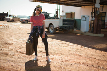 Woman in twenties standing on red-dirt forecourt wearing red T-shirt holding jerry can near pickup © wavebreak3