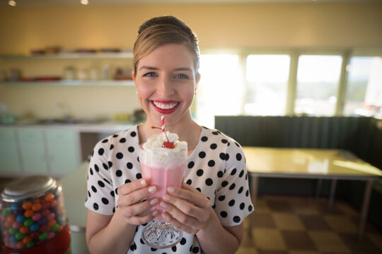 Pink milkshake sitting in footed glass on yellow diner table near window, gumball machine glowing